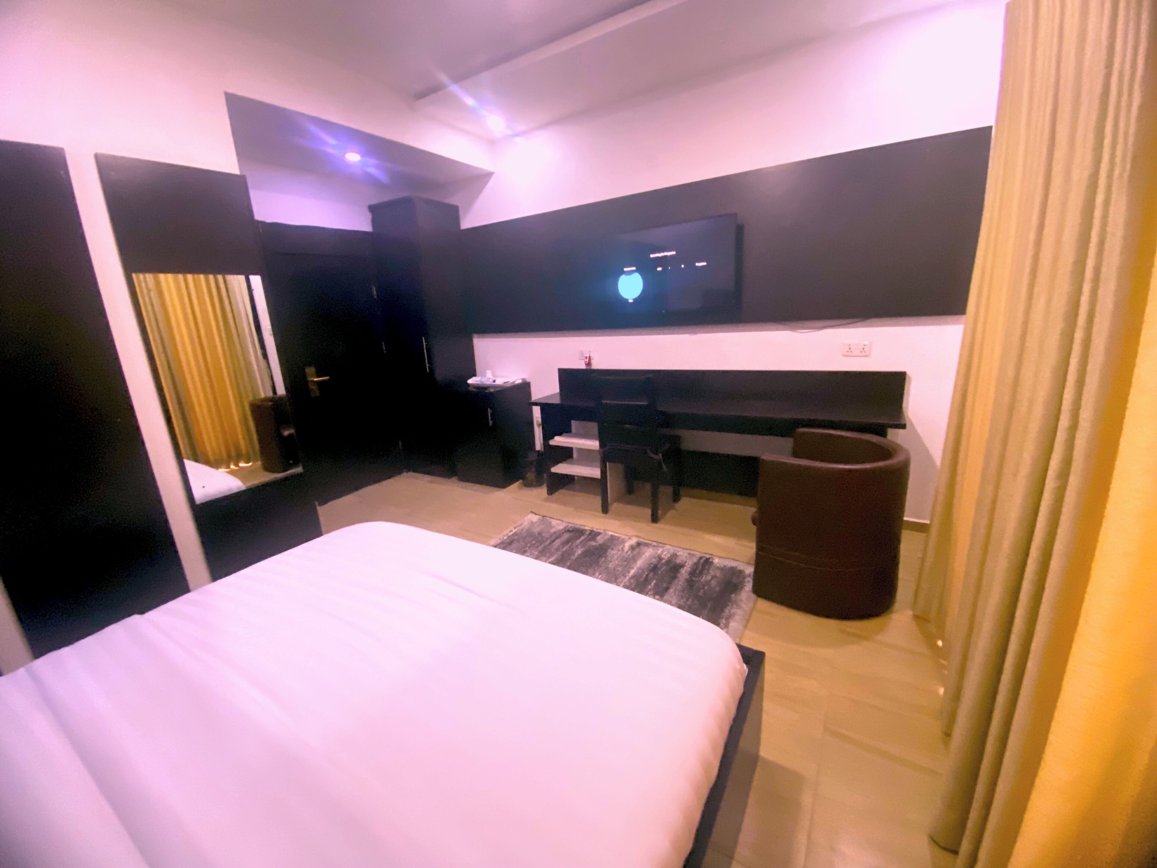 A modern hotel room with a large bed, a desk, a chair, a television, and a bathroom.