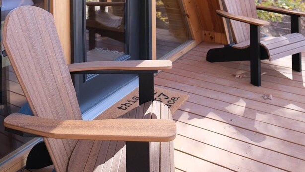 Una terraza de madera con dos sillas Adirondack y una puerta de cristal que da a un espacio interior.