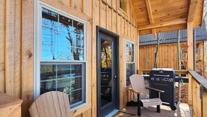 A wooden deck with a grill and chairs, large windows, and a door. - Kenai Fjord/Lakeview 4-6 Person Midsize Cabin (Franklin Township)