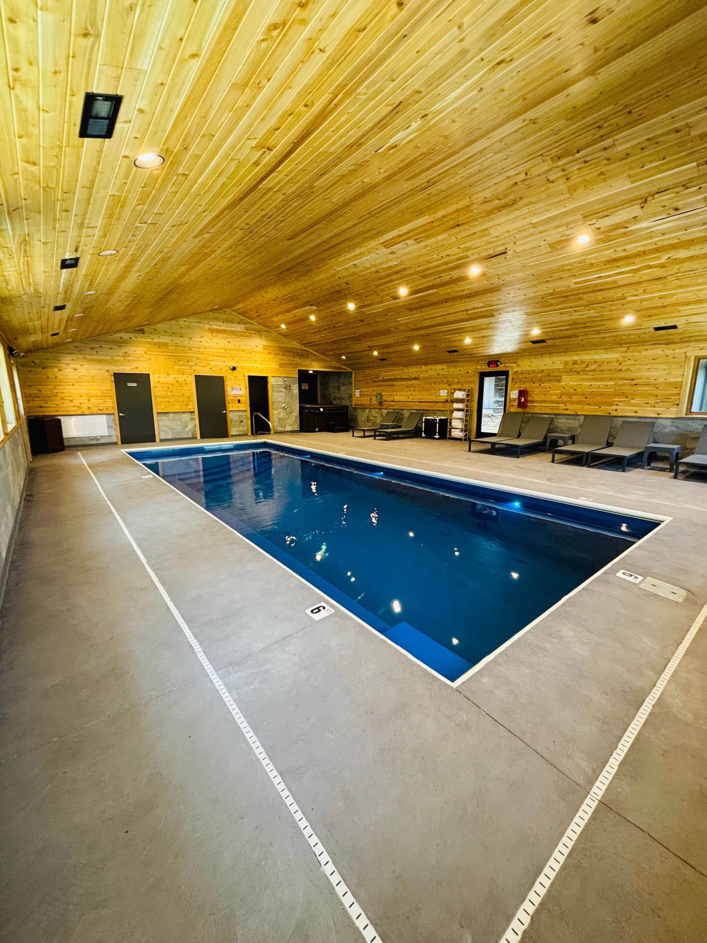An indoor swimming pool with wooden walls and ceiling, seating areas, and a lifeguard station.