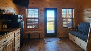 A cozy cabin interior with wooden walls, a wooden ceiling, a built-in bench, a sofa, a kitchen area with a microwave, and a TV mounted on the wall. - Kenai Fjord/Lakeview 4-6 Person Midsize Cabin (Franklin Township)