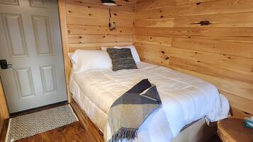 A wooden cabin room with a bed, a nightstand, a lamp, and a door.