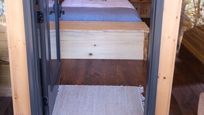 Uma cabana de madeira aconchegante, com uma cama, uma mesinha e uma luminária no teto.