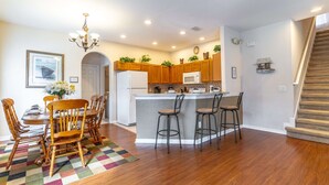 Una cocina moderna con armarios de madera, una isla central, taburetes de bar y una zona de comedor con mesa y sillas de madera.