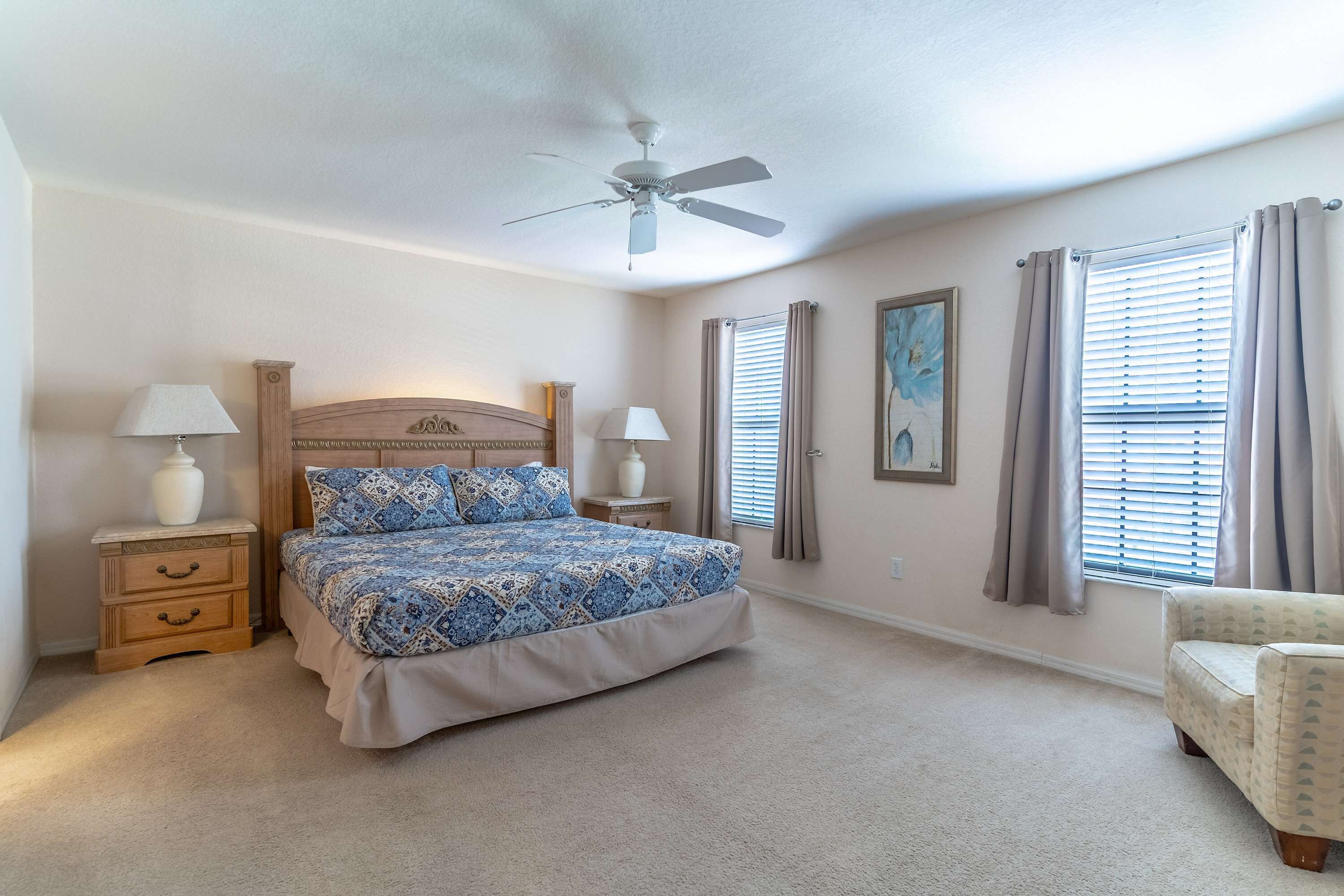 A bedroom with a bed, nightstands, a ceiling fan, a window with blinds, and a chair.