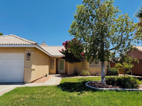 A residential house with a garage, a well-maintained lawn, and a tree with pink flowers.