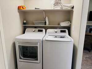 A laundry area with two white front-loading washing machines and a shelf above containing folded towels and a box of laundry detergent.