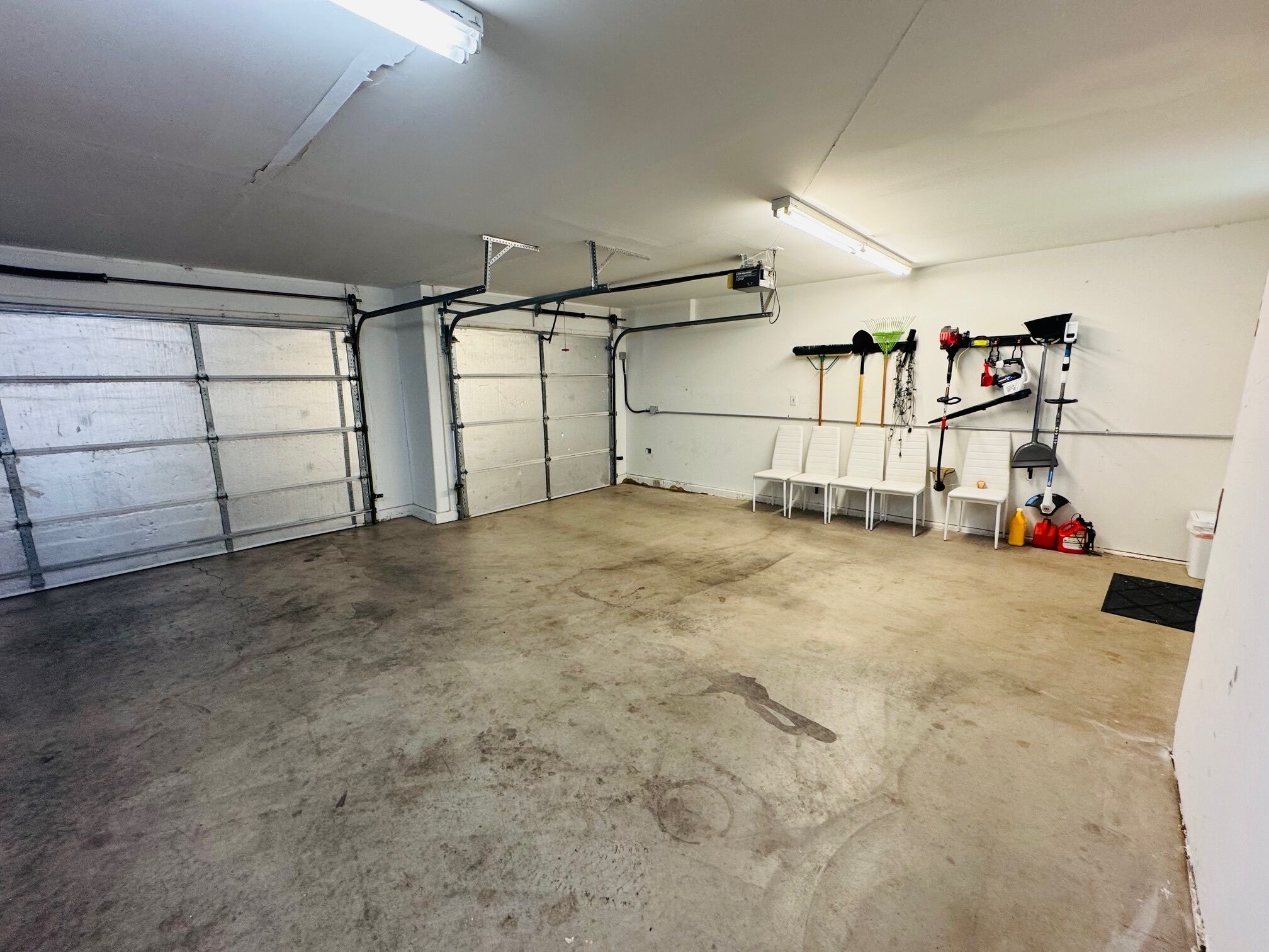 A garage with four white garage doors, a concrete floor, and a wall-mounted tool rack with various tools.