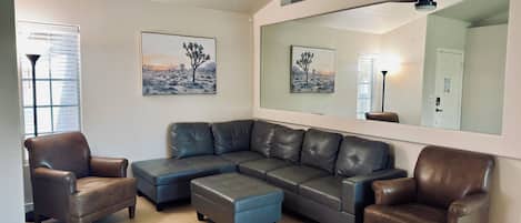 Ein Wohnzimmer mit einem Ecksofa, zwei Sesseln, einem Couchtisch, einem Deckenventilator und Kunstwerken an den Wänden.