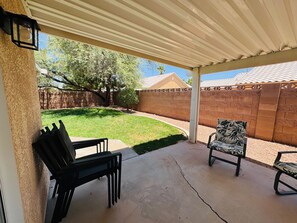 A covered patio with a concrete floor, two black chairs, and a patterned chair.