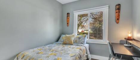 A bedroom with a bed, a desk, and a window.