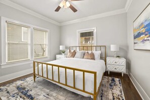 Une chambre à coucher comprenant un lit, des tables de chevet, un ventilateur de plafond et une fenêtre avec des stores.