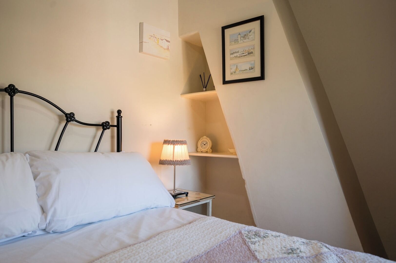 Une chambre à coucher avec un lit en métal, une lampe de chevet, une horloge et un tableau encadré au mur.