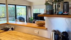 Una cucina moderna con ripiani in legno, un bollitore, una macchina da caffè e una ciotola sul piano di lavoro. Si vede una finestra con vista sul verde.