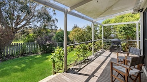 Veranda coperta con barbecue, sedie e vista su un giardino.