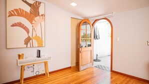 A room with wooden flooring, a white console table with a decorative item, a framed artwork, and a wooden door leading outside. - Santa Lucia Suites - Barranco (Cuenca)