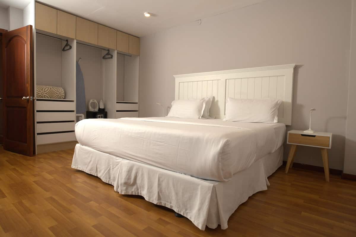A bedroom with a large bed, wooden flooring, a wardrobe, and a bedside table.