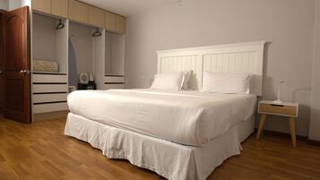 A bedroom with a large bed, wooden flooring, a wardrobe, and a bedside table.