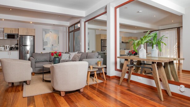 A spacious living area with a sofa, coffee table, and a dining table with chairs. There is a kitchen in the background with modern appliances. - Santa Lucia Suites - Barranco (Cuenca)