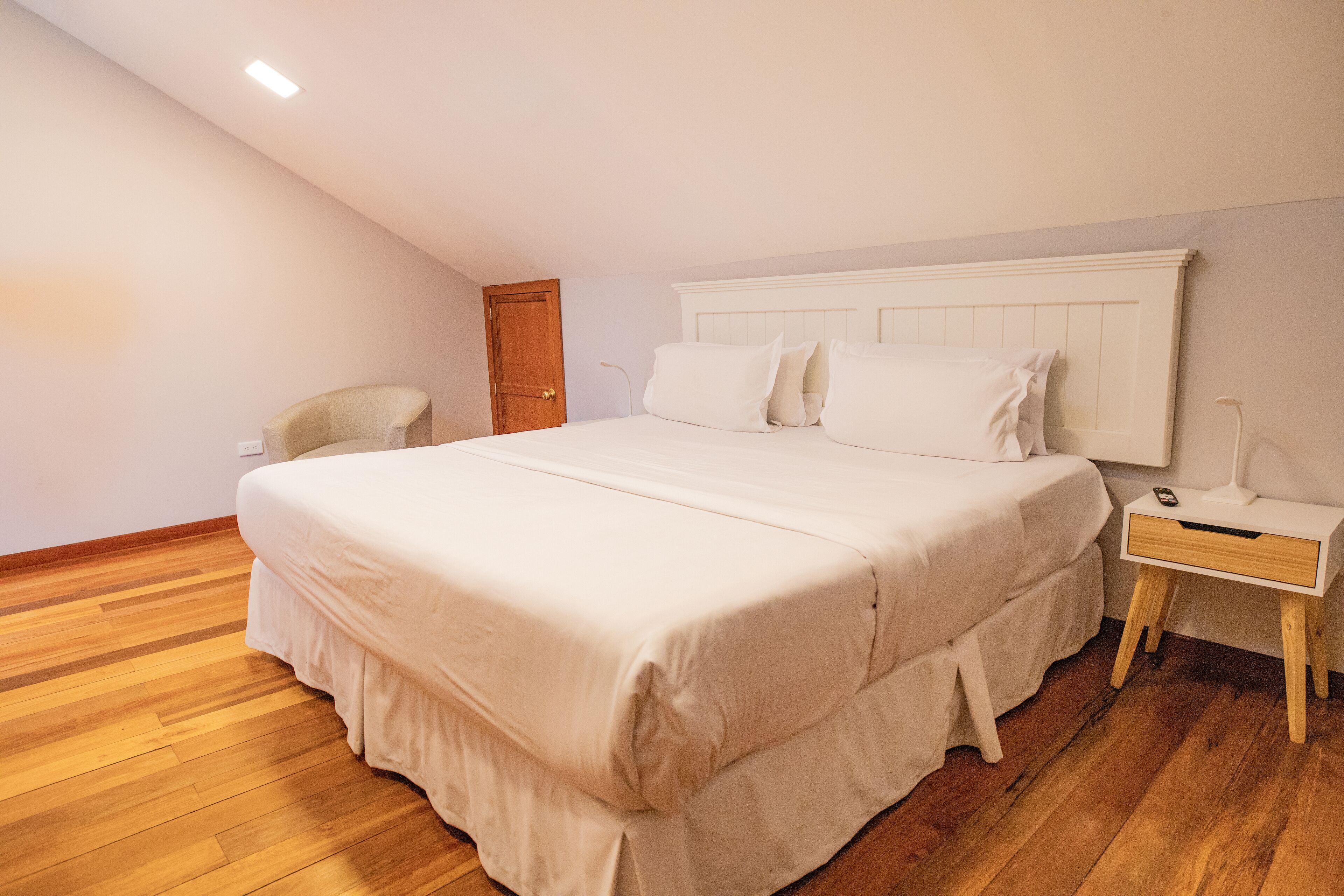 A bedroom with a large bed, a bedside table, a chair, and a wooden floor.