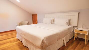 A bedroom with a large bed, a bedside table, a chair, and a wooden floor.
