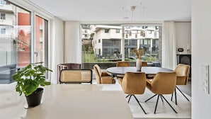 A modern dining area with a round table, six chairs, and a potted plant.