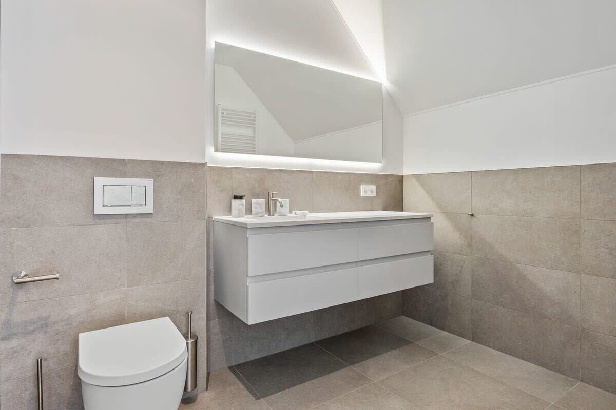 Ein modernes Badezimmer mit einem weißen Waschtisch, einem großen Spiegel und einer Toilette.