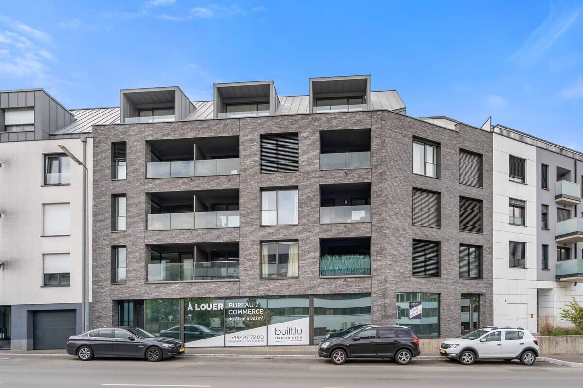 Edificio a più piani con piano terra ad uso commerciale, con insegna che riporta 'A LOUER BUREAU / COMMERCE' e 'built.lu IMMOBILIER'.