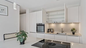 A modern kitchen with white cabinetry, a built-in oven, a stovetop, and a glass shelf above the sink.