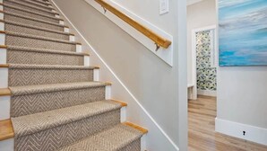 A staircase with a herringbone carpet pattern, wooden handrails, and a light-colored wall. - Steps to Ice Plant, in Downtown St Augustine (St. Augustine)
