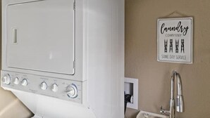 A white washing machine with control knobs, a sign on the wall that reads "Laundry Company Same Day Service", and a modern faucet.