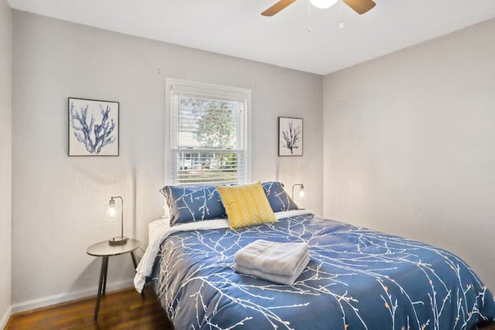 A bedroom with a bed, a window, a ceiling fan, and two wall-mounted lamps.