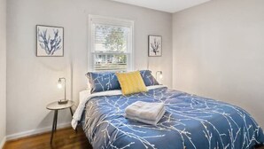 A bedroom with a bed, a window, a ceiling fan, and two wall-mounted lamps.