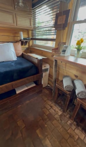 Ein gemütliches Blockhausszimmer mit Bett, kleinem Tisch, Heizung und Fenster mit Jalousien.