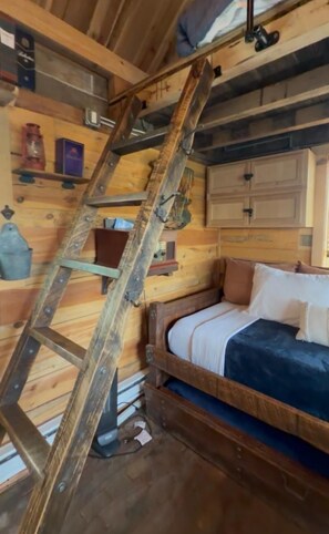 A wooden cabin interior with a bunk bed, a ladder, and a wooden ceiling.