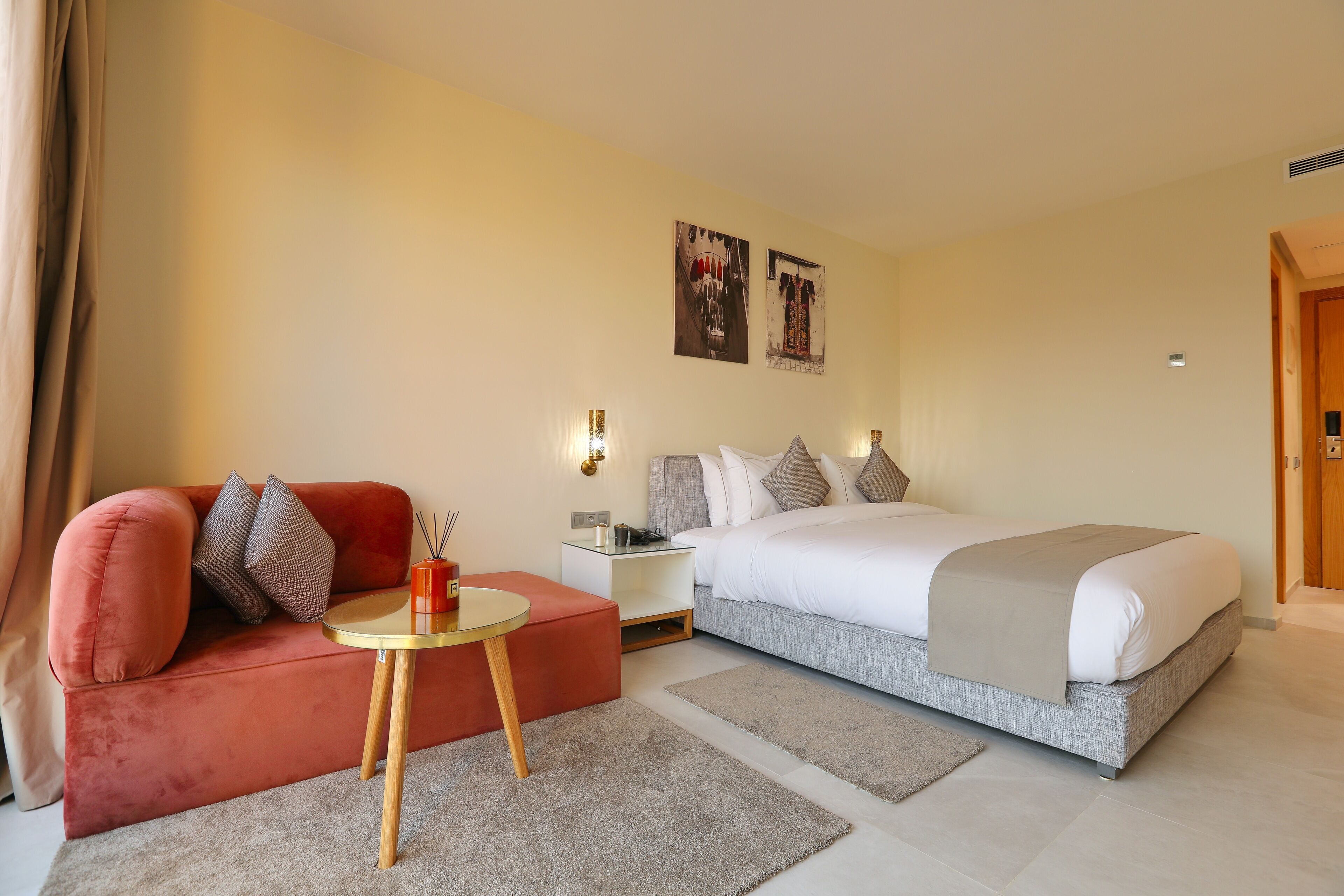 A hotel room with a bed, a red sofa, a small round table, and two wall-mounted lamps.