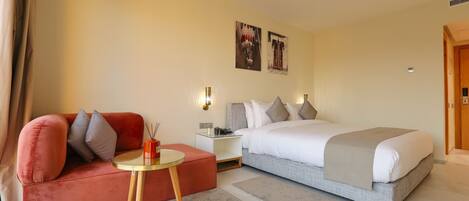 A hotel room with a bed, a red sofa, a small round table, and two wall-mounted lamps.