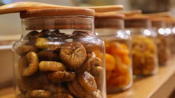Una fila de frascos de vidrio con tapas, sobre una estantería de madera, que contienen diversas frutas secas.