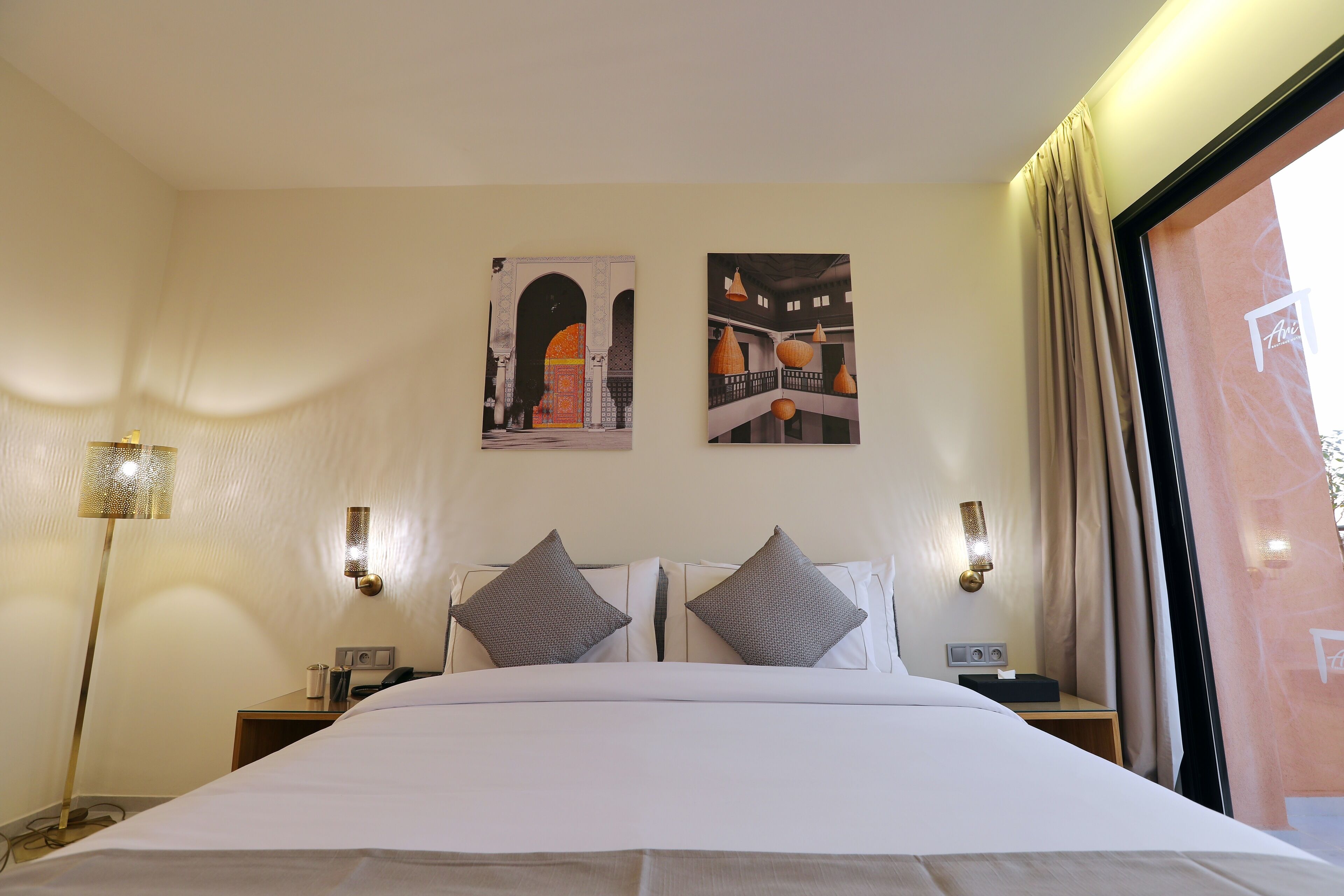 A hotel room with a large bed, two wall-mounted lamps, and two paintings.