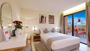 Ein Hotelzimmer mit einem großen Bett, einem Schreibtisch mit Stuhl, einem Spiegel und Blick ins Freie.