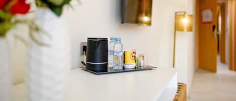 A hotel reception desk with a vase of red roses, a black kettle, water bottles, a yellow mug, and a small container.