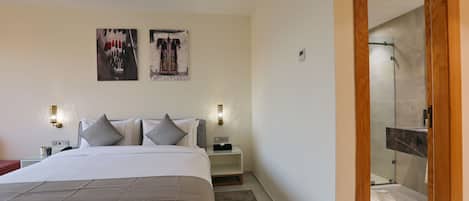 A modern bedroom with a large bed, two bedside tables, and a nightstand. There are two wall-mounted light fixtures and two framed artworks above the bed.