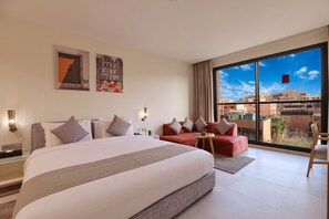 A modern hotel room with a large bed, a red sofa, a small table, and a large window offering a city view. - Ari Boutique Hotel - Adults Only (Marrakech)