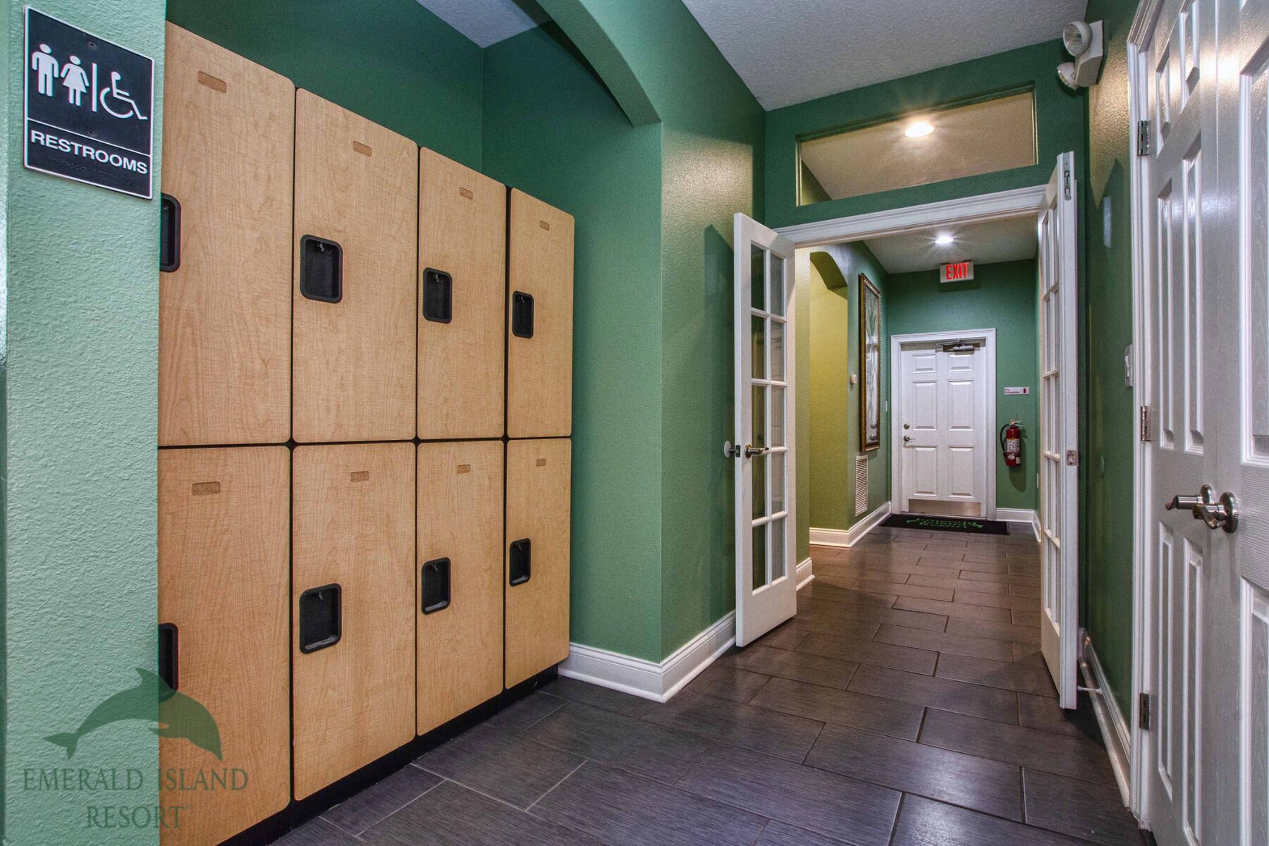 A hallway with wooden lockers, a sign for restrooms, and a door marked "EXIT".
