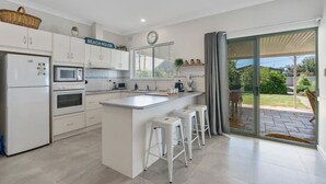 Una cocina moderna con armarios blancos, una isla central con taburetes, microondas, horno y un letrero que dice 'BEACH HOUSE'.