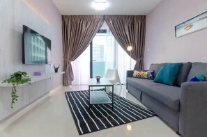 A modern living room with a grey sofa, a black and white striped rug, a flat-screen TV mounted on the wall, and a large window with curtains.