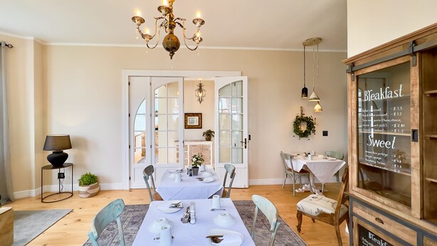 A dining area with a table set for four, a chandelier, and a menu board on the wall. - Brigadoon Boutique Guesthouse l Ondili (Swakopmund)