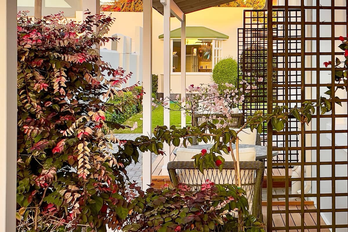 Un espacio al aire libre techado con una pérgola, una zona de estar y vistas a un edificio con tejado verde.