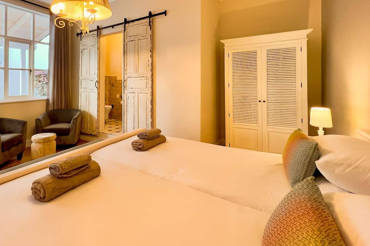 Habitación de hotel con cama, dos sillones, una mesita redonda, espejo, armario y ventana con cortinas.