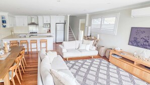 A modern kitchen with white cabinets, a dining area with a wooden table and chairs, a white sofa, and a patterned rug.
